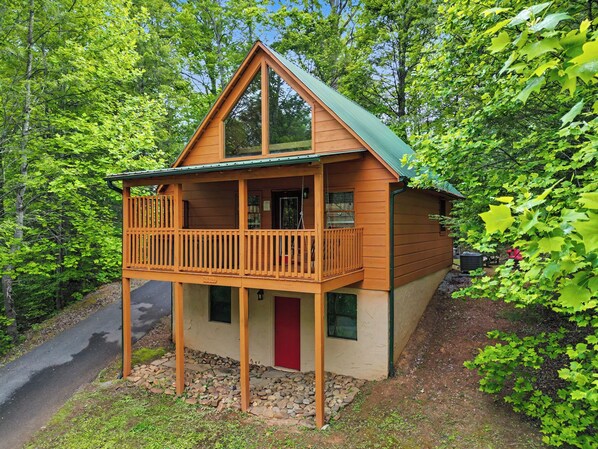 A cabin with a balcony, surrounded by trees.