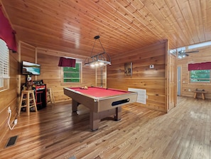 Une table de billard recouverte d’un drap de feutre rouge, un téléviseur fixé au mur et une fenêtre donnant sur l’extérieur.