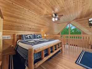 A wooden cabin bedroom with a bed, a ceiling fan, and a large window.