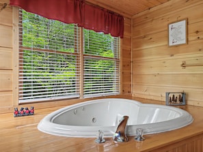 L’intérieur d’un chalet en bois, avec une grande baignoire ovale, une fenêtre avec des stores et une citation encadrée accrochée au mur.