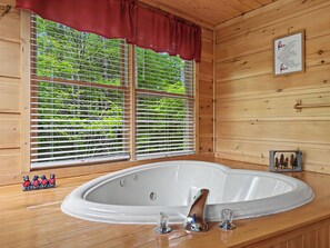 A wooden cabin interior with a large oval bathtub, a window with blinds, and a framed quote on the wall.