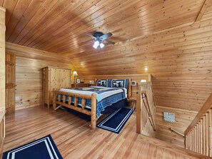 Un dormitorio de cabaña de madera con cama, ventilador de techo y escalera de madera.