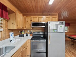 A kitchen with wooden cabinets, a stainless steel refrigerator, a microwave, an oven, and a sink.