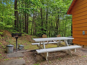 A picnic table set up in a forested area with a cabin in the background.