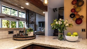A kitchen with granite countertops, wooden cabinets, a stone wall, and a large window. - Sunset View over Lake Whatcom with Hot Tub! (Bellingham)