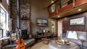A living room with a stone fireplace, a guitar, a sofa, and a television. - Sunset View over Lake Whatcom with Hot Tub! (Bellingham)