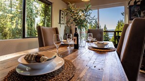 A dining table with plates, glasses, and a bottle, set against a window with a view of trees. - Sunset View over Lake Whatcom with Hot Tub! (Bellingham)