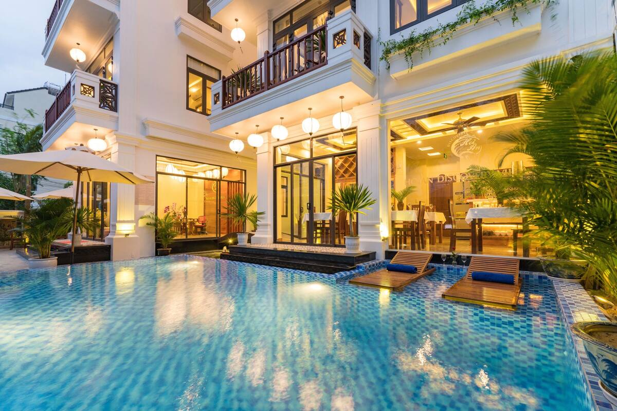 A hotel with a swimming pool, outdoor seating, and a well-lit entrance.