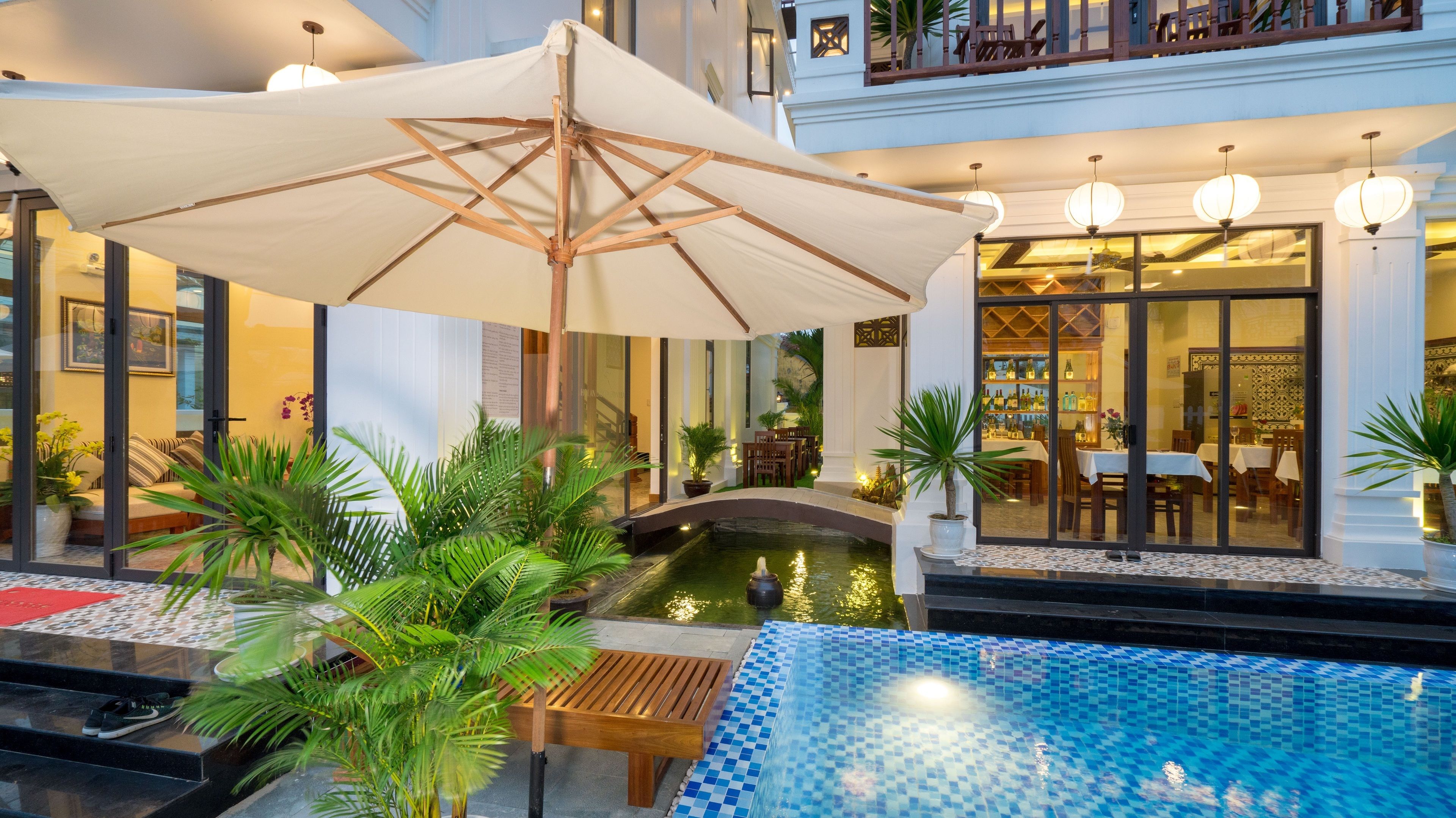 A pool area with a small bridge, surrounded by potted plants and a wooden bench.