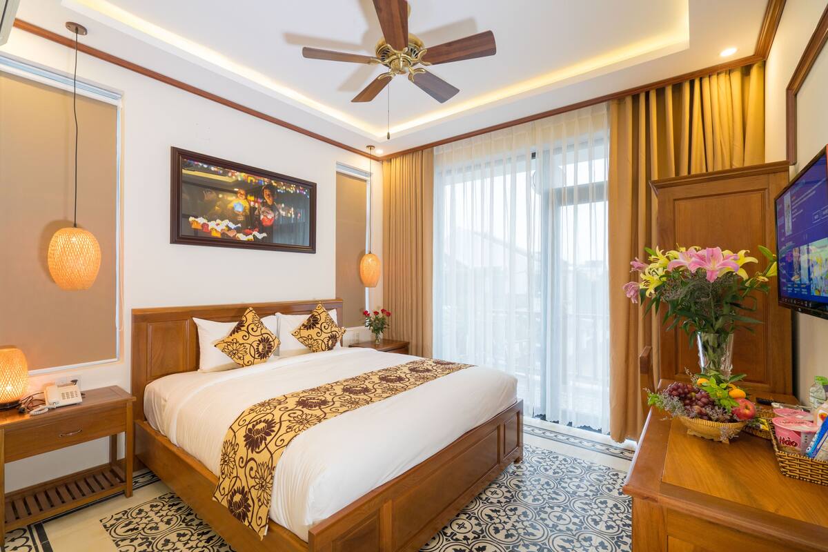 A hotel room with a large bed, a ceiling fan, a TV, and a window with curtains.