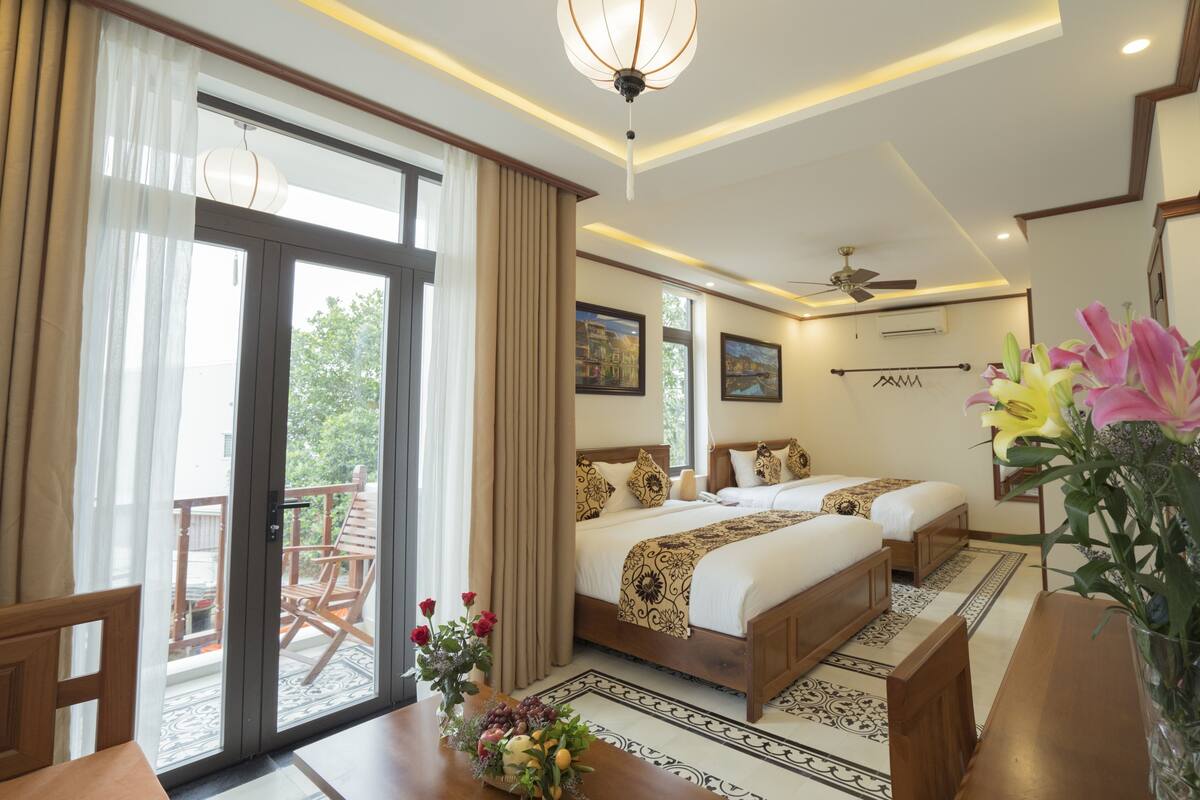 A hotel room with a large sliding glass door to the balcony, a bed with a patterned bedspread, a ceiling fan, and a vase with flowers on the table.