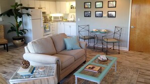 Un salon avec un canapé beige, une table basse en verre et un coin repas comprenant deux chaises.