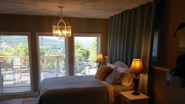 Une chambre avec un grand lit, deux lampes de chevet, une table de chevet et une vue sur un balcon aménagé avec du mobilier d’extérieur.