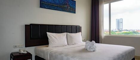 A hotel room with a bed, a painting, a view of a cityscape, and a telephone on a nightstand.