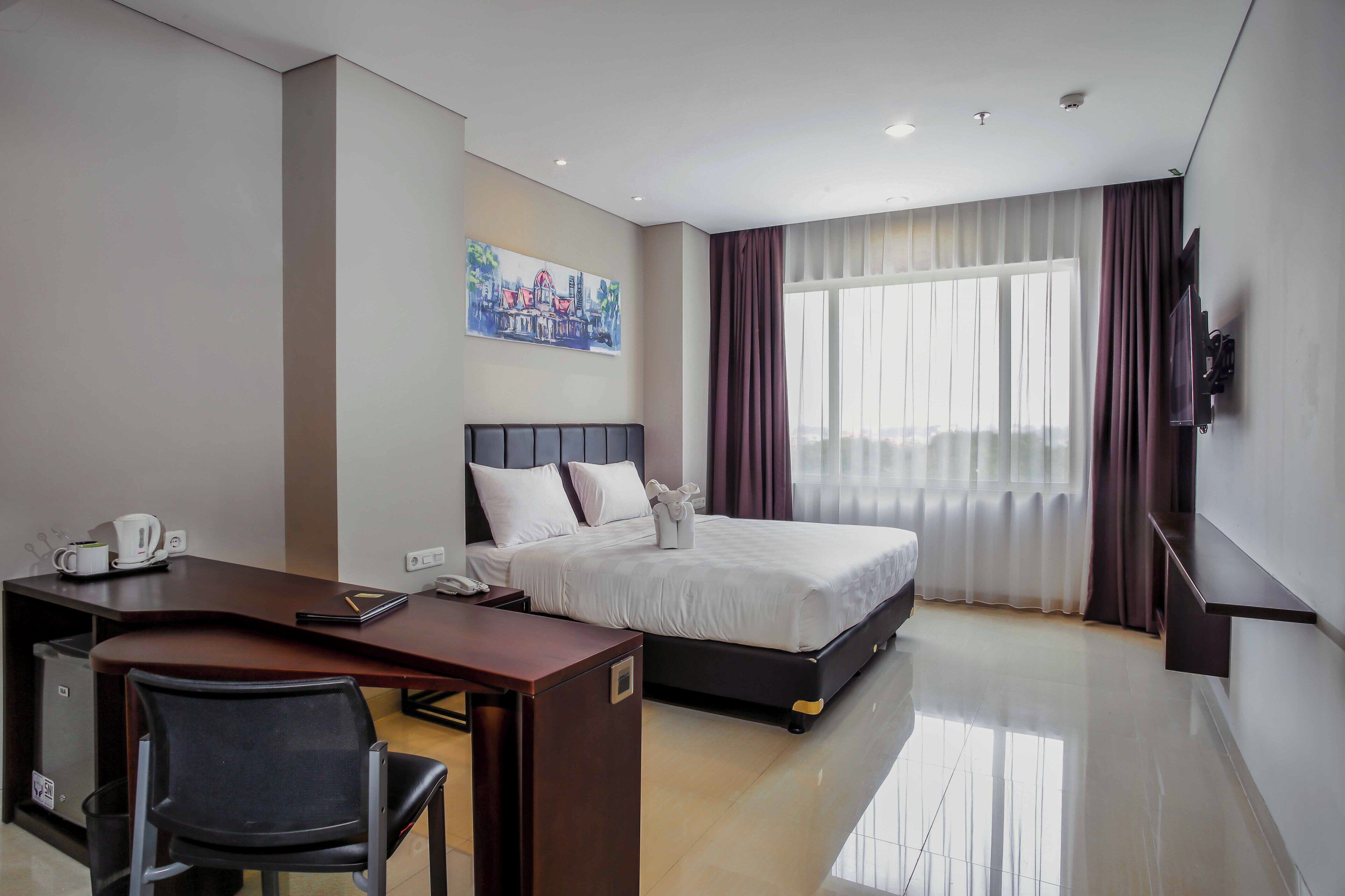 Una habitación de hotel con cama, escritorio, silla y un cuadro en la pared.