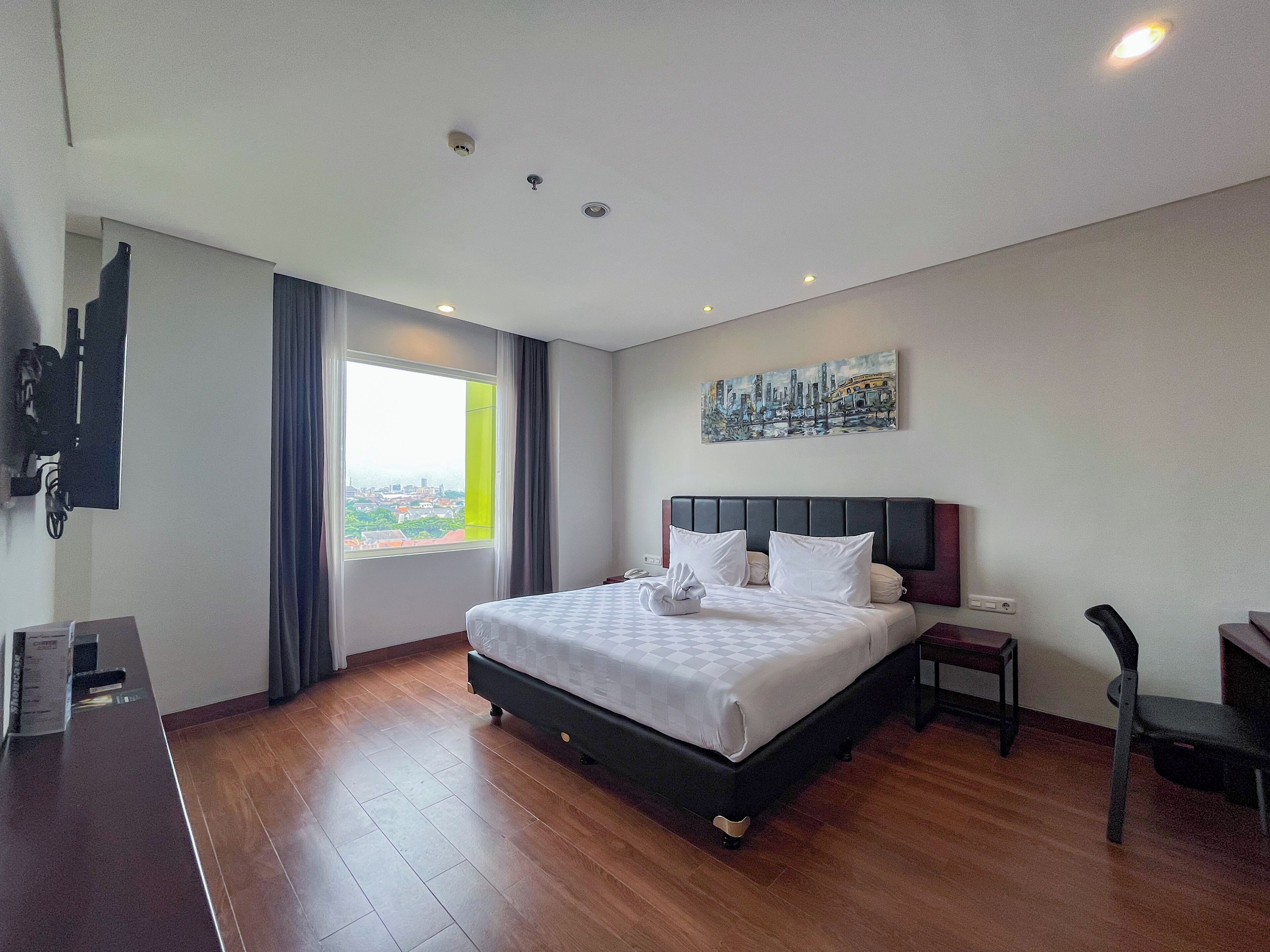 A hotel room with a bed, a desk, a chair, a TV, a painting, and a window with a view.