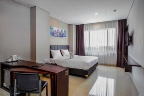 A hotel room with a bed, desk, chair, and a painting on the wall. - PrimeBiz Hotel Surabaya (Surabaya)