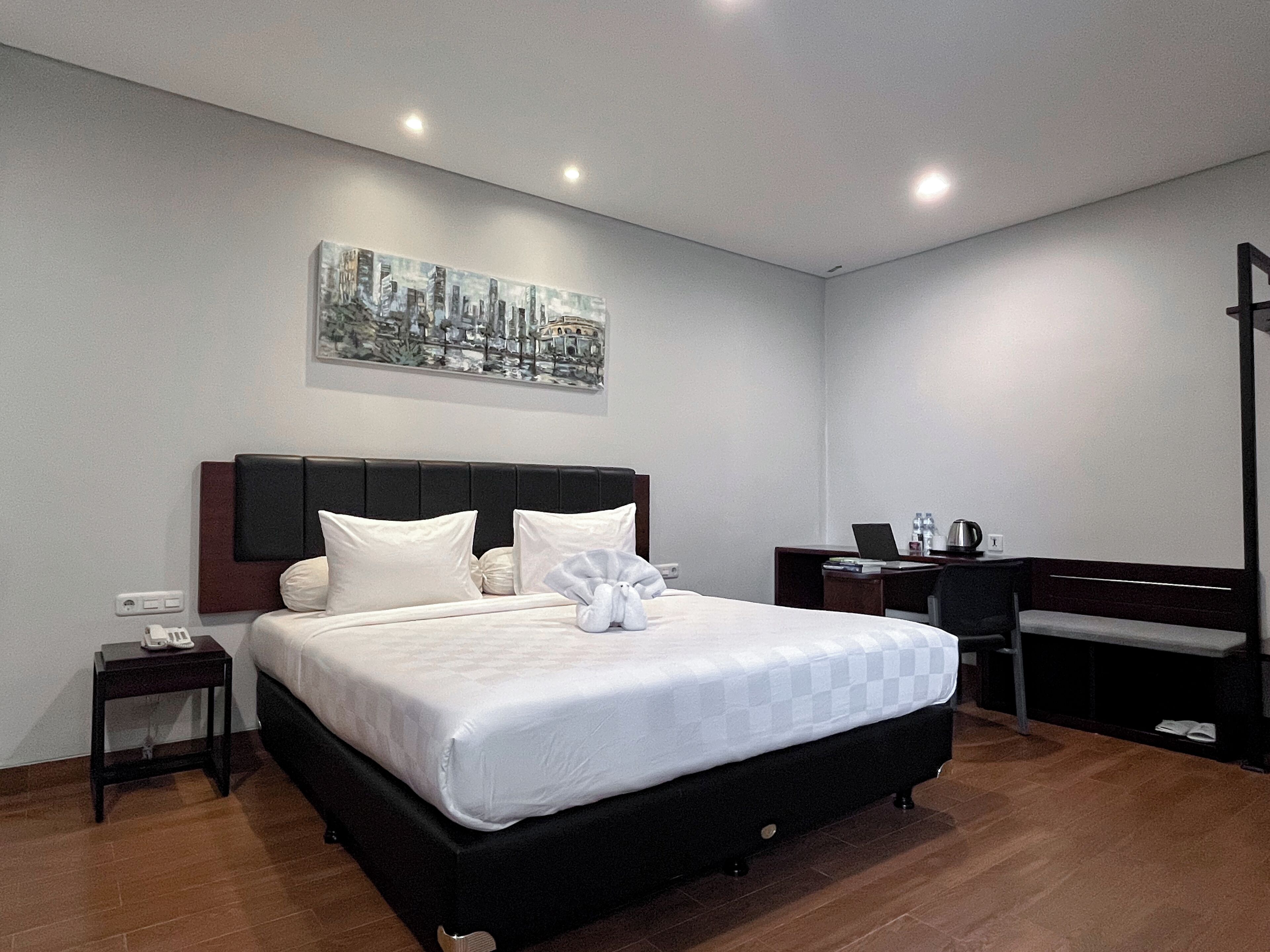 A modern hotel room with a large bed, a desk, a chair, and a painting on the wall.