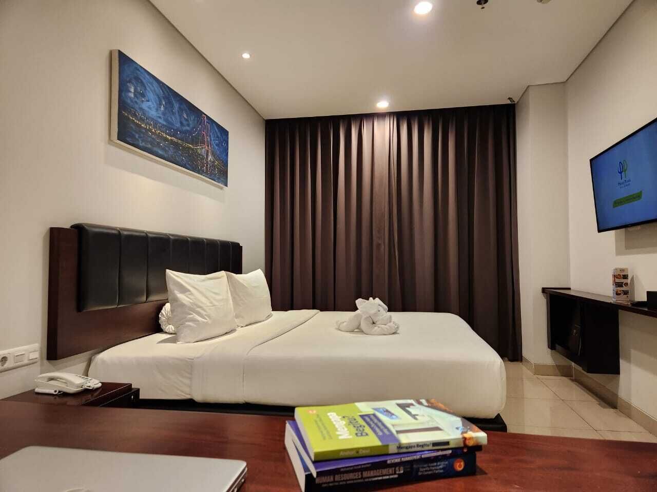 Habitación de hotel con una cama, un televisor de pantalla plana, una estantería y un cuadro en la pared.