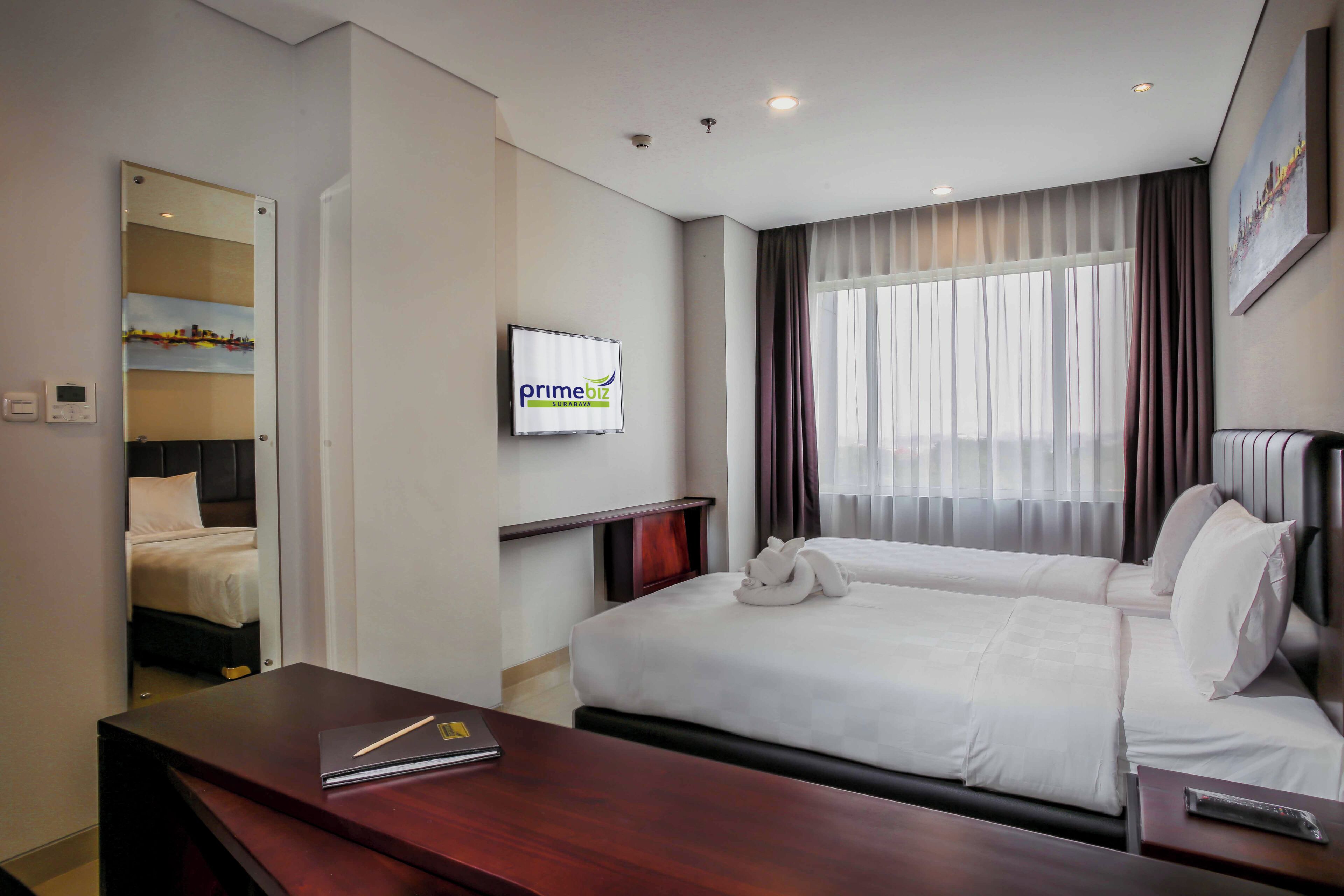 A hotel room with a bed, bedside tables, a TV, and a window with curtains.