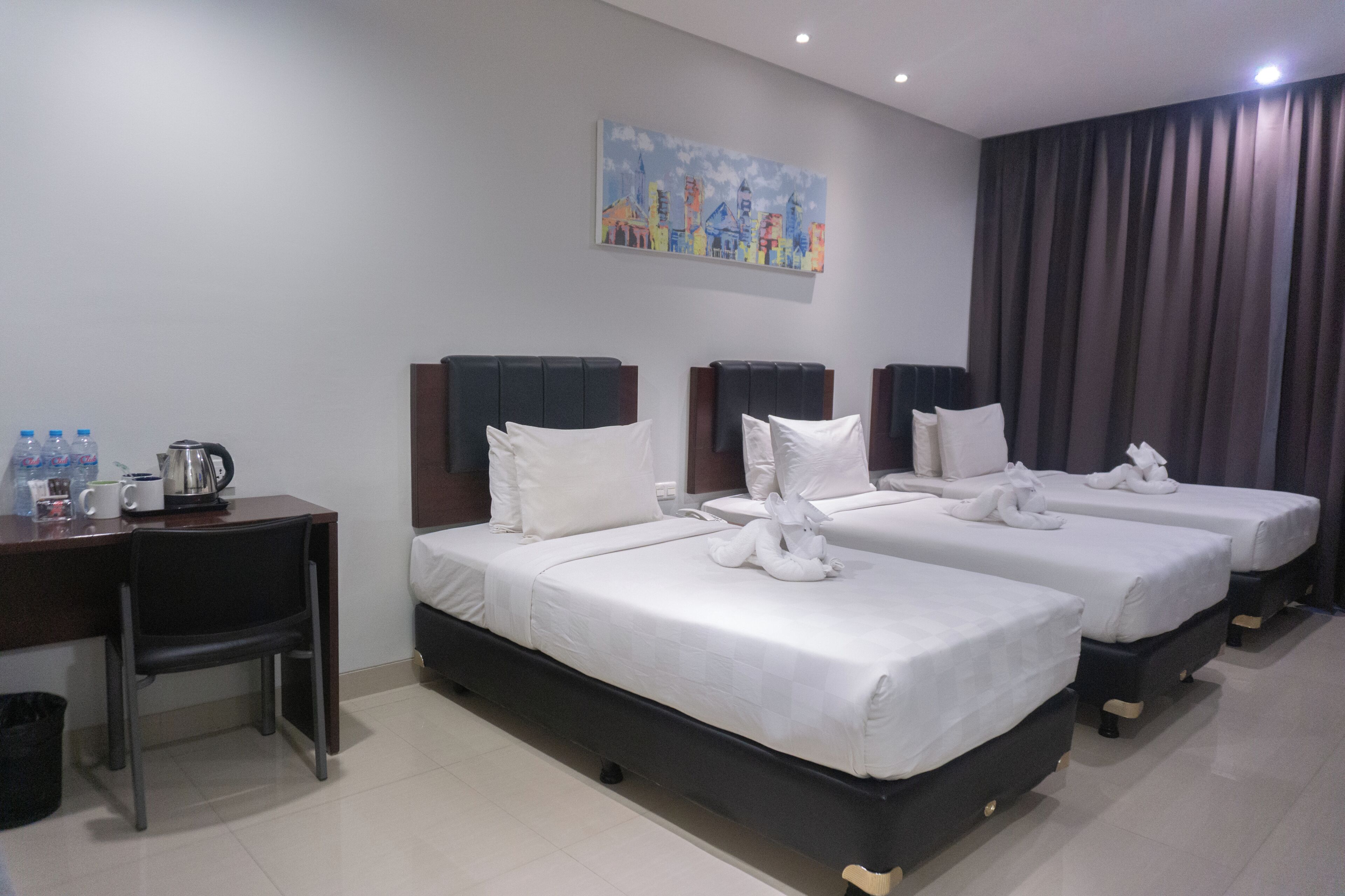 A hotel room with two beds, a desk, a chair, a painting on the wall, and a curtain.