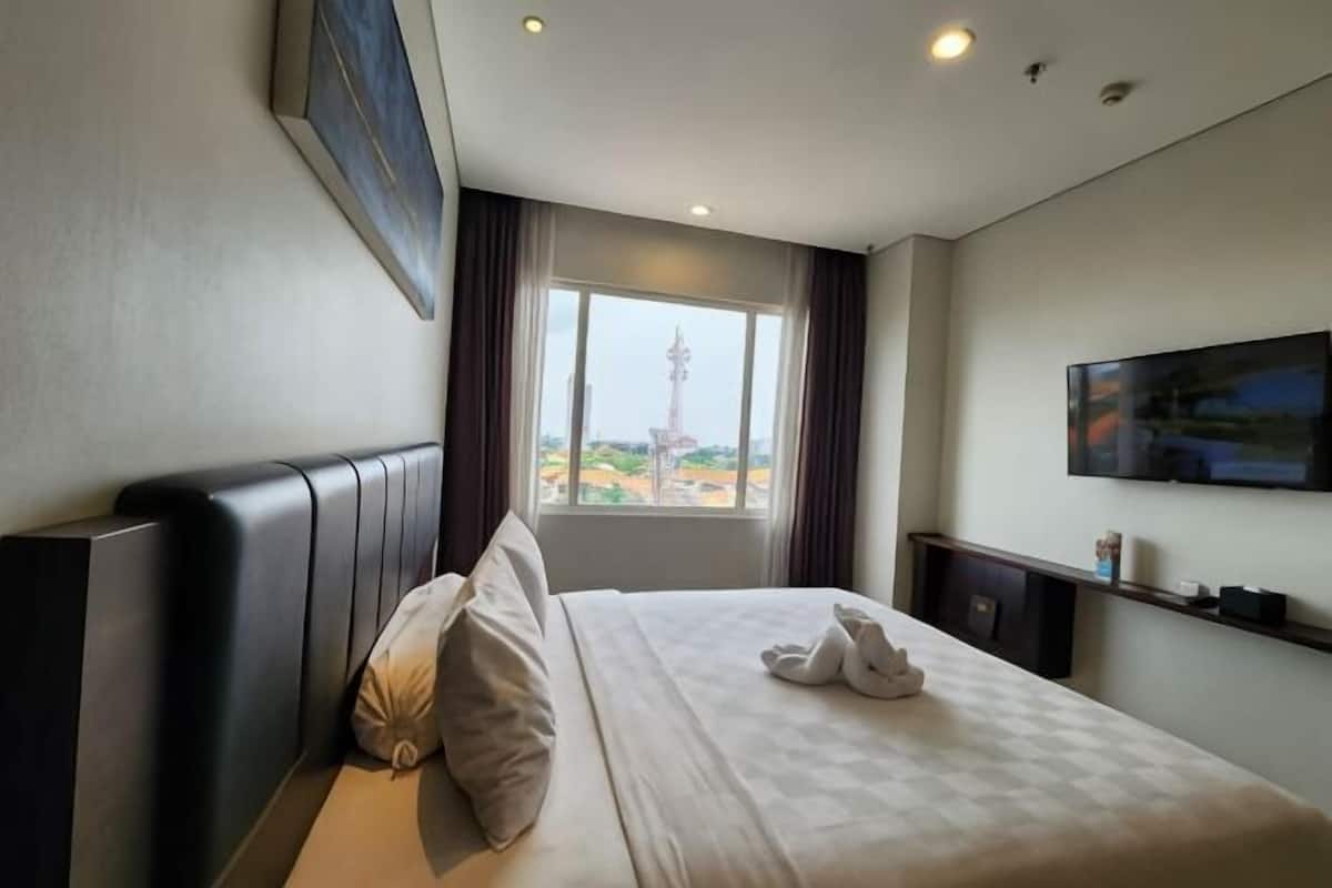 A hotel room with a bed, a window with a view, a television, and a painting on the wall.