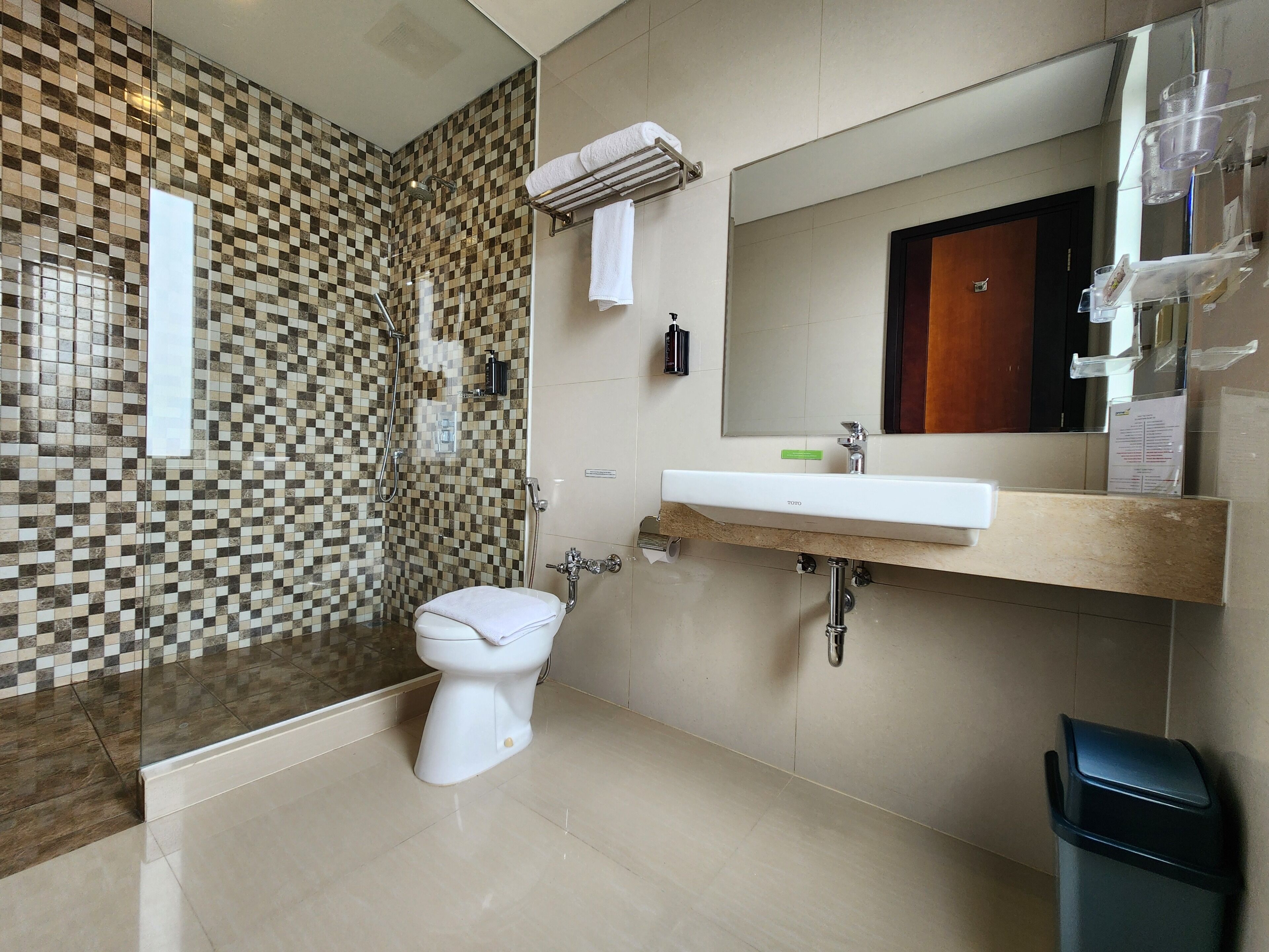 A bathroom with a checkered tile wall, a toilet, a sink with a mirror, and a trash bin.
