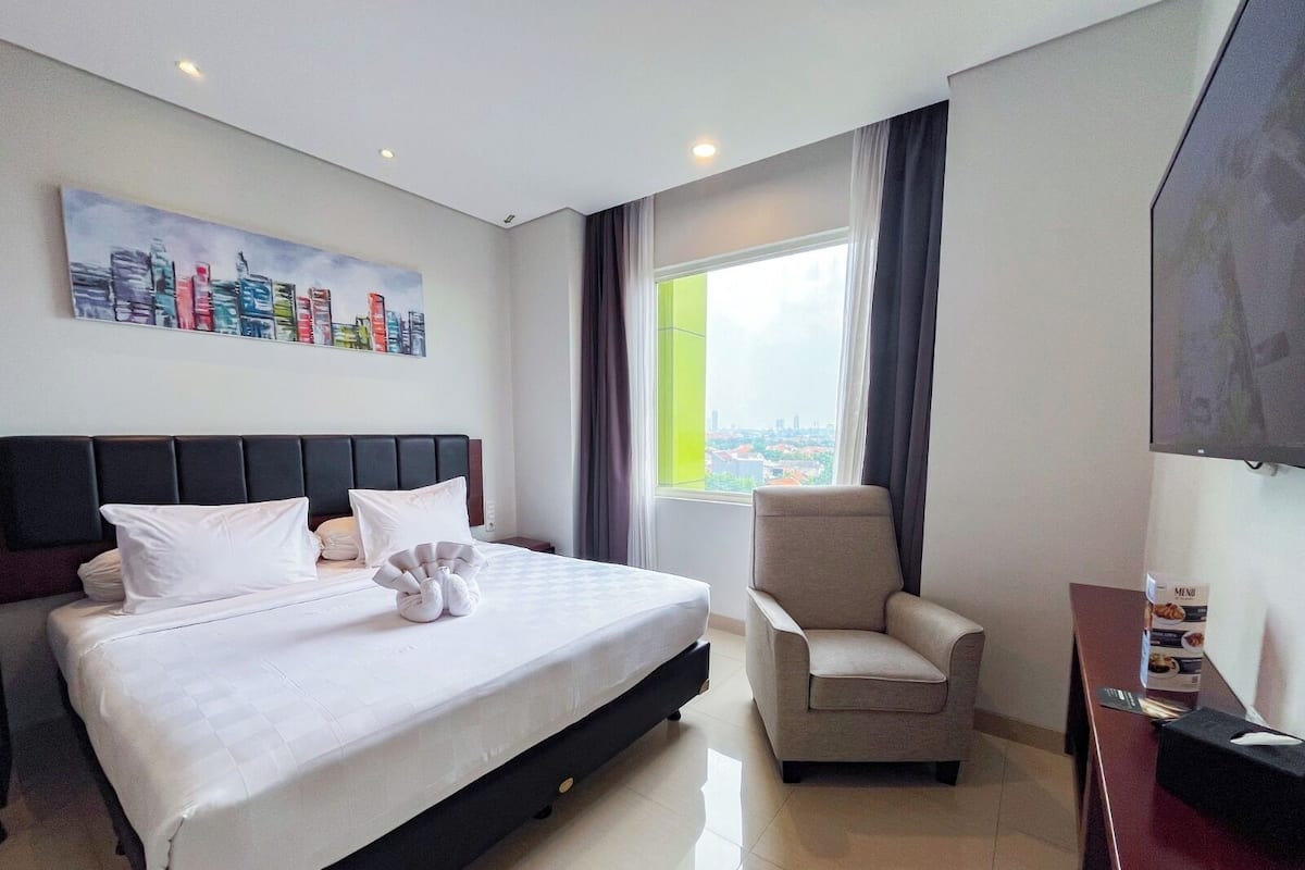 A hotel room with a bed, a chair, a TV, and a window with a view.