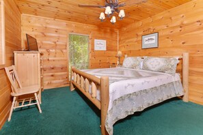 A wooden cabin room with a bed, a desk, and a chair.