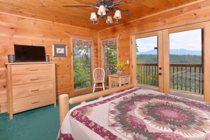 A wooden cabin bedroom with a bed, dresser, TV, and a view of the outdoors. - Great Mountain View | Next to Dollywood | Pool Table | Pet Friendly | Hot Tub (Pigeon Forge)
