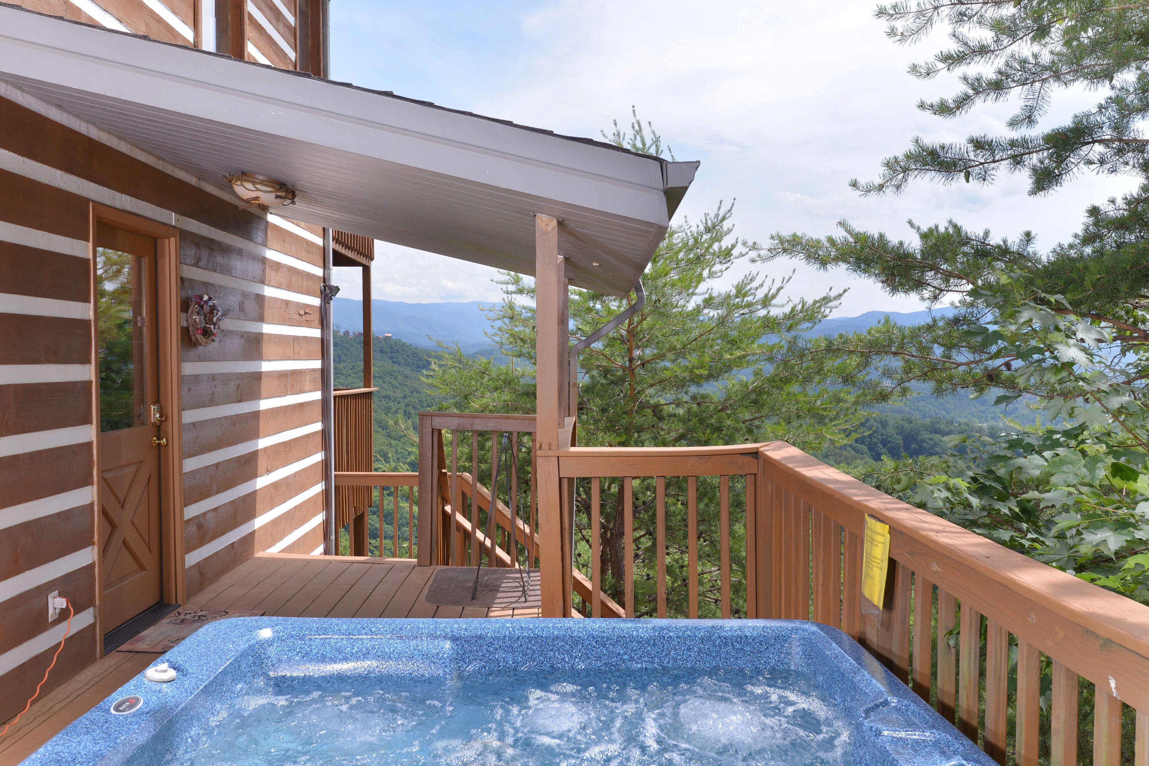 Una terraza de madera con un jacuzzi, una puerta de madera y vistas a las montañas.