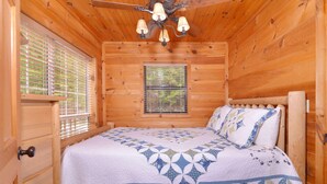 A wooden cabin bedroom with a bed, a window with blinds, and a ceiling fan. - Great Mountain View | Next to Dollywood | Pool Table | Pet Friendly | Hot Tub (Pigeon Forge)