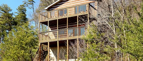 A two-story wooden cabin with a balcony, surrounded by trees.