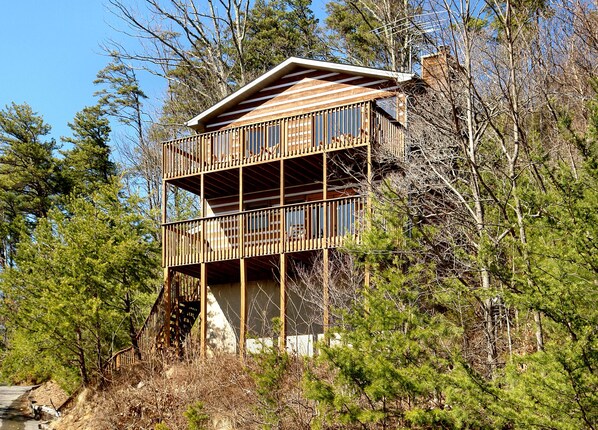 A two-story wooden cabin with a balcony, surrounded by trees. - Great Mountain View | Next to Dollywood | Pool Table | Pet Friendly | Hot Tub (Pigeon Forge)
