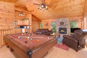 Ein Holzhütten-Interieur mit Pooltisch, Ledersofa und Kamin.