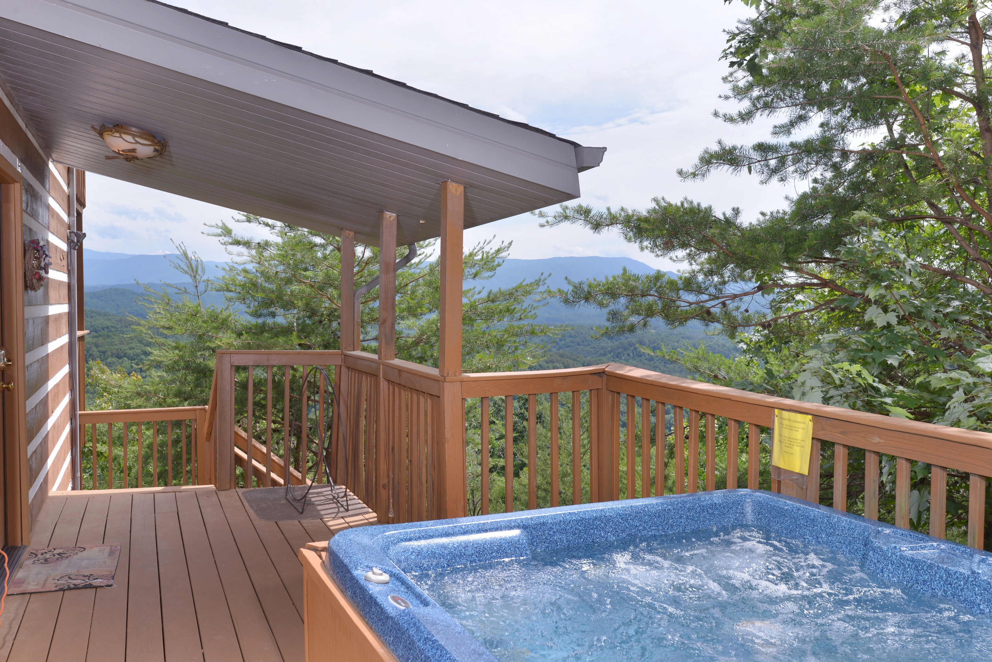 Une terrasse en bois avec un jacuzzi, offrant une vue sur un paysage montagneux.