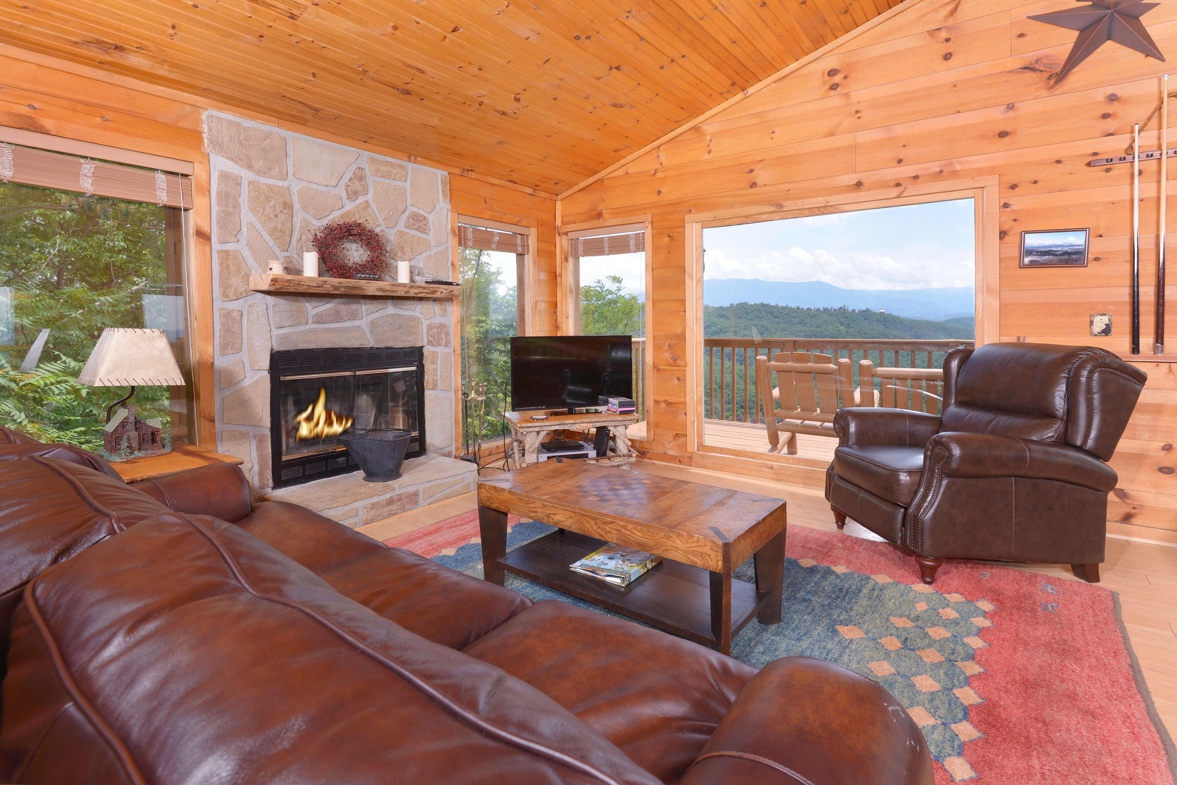 A cozy cabin interior with a stone fireplace, leather sofa, and a television.