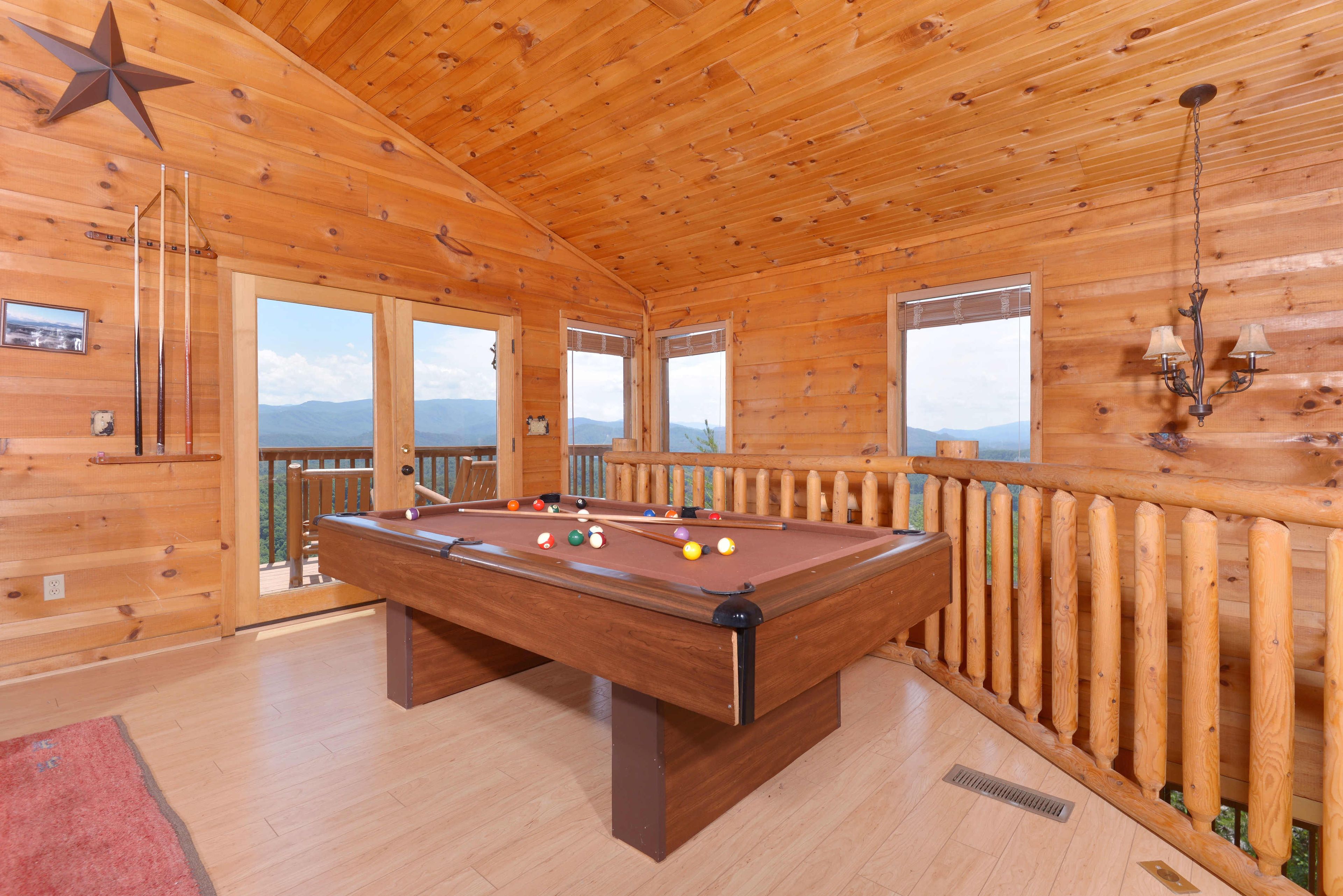 A wooden pool table in a room with large windows and a balcony.