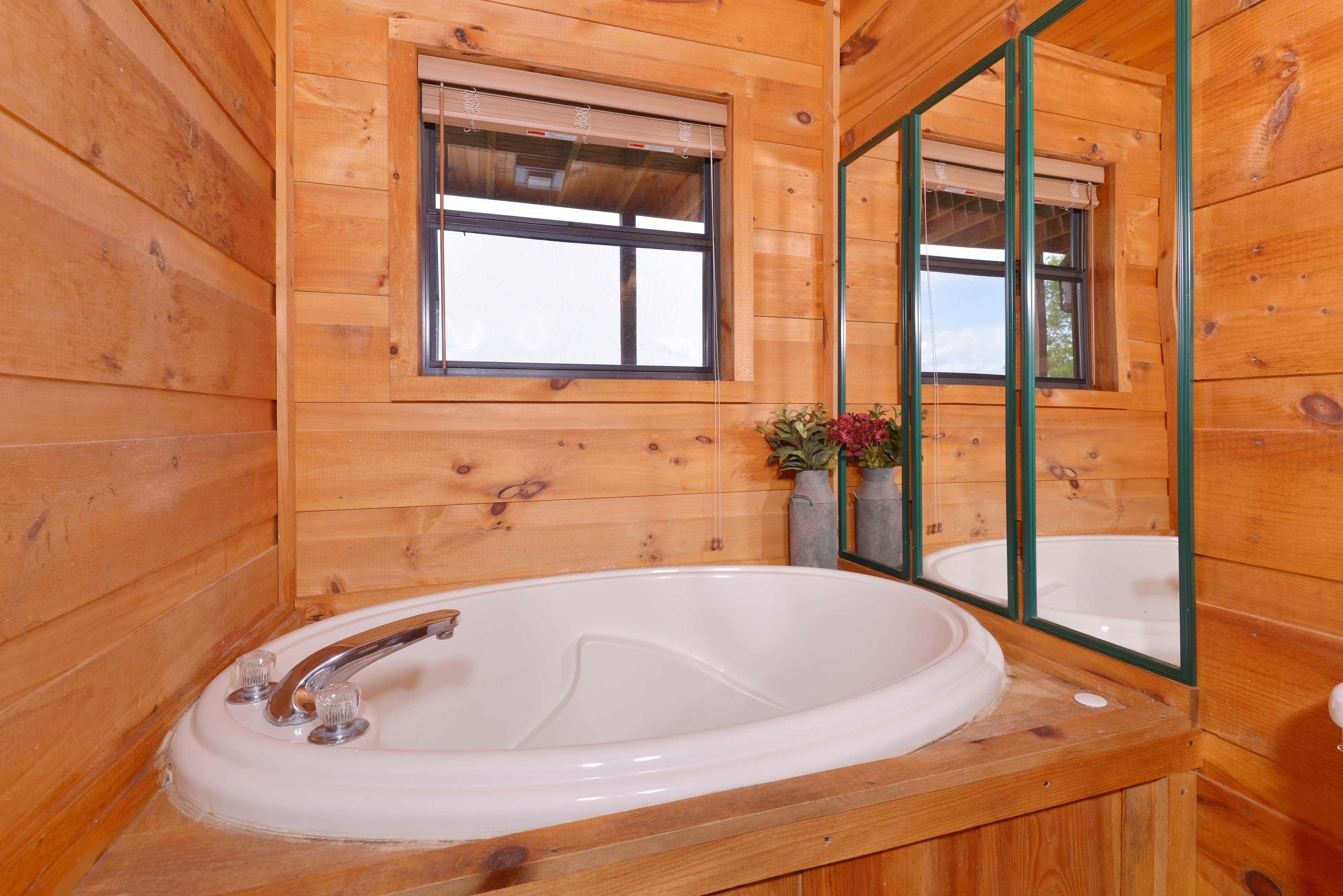 A wooden cabin bathroom with a large bathtub, a window, and a mirror.