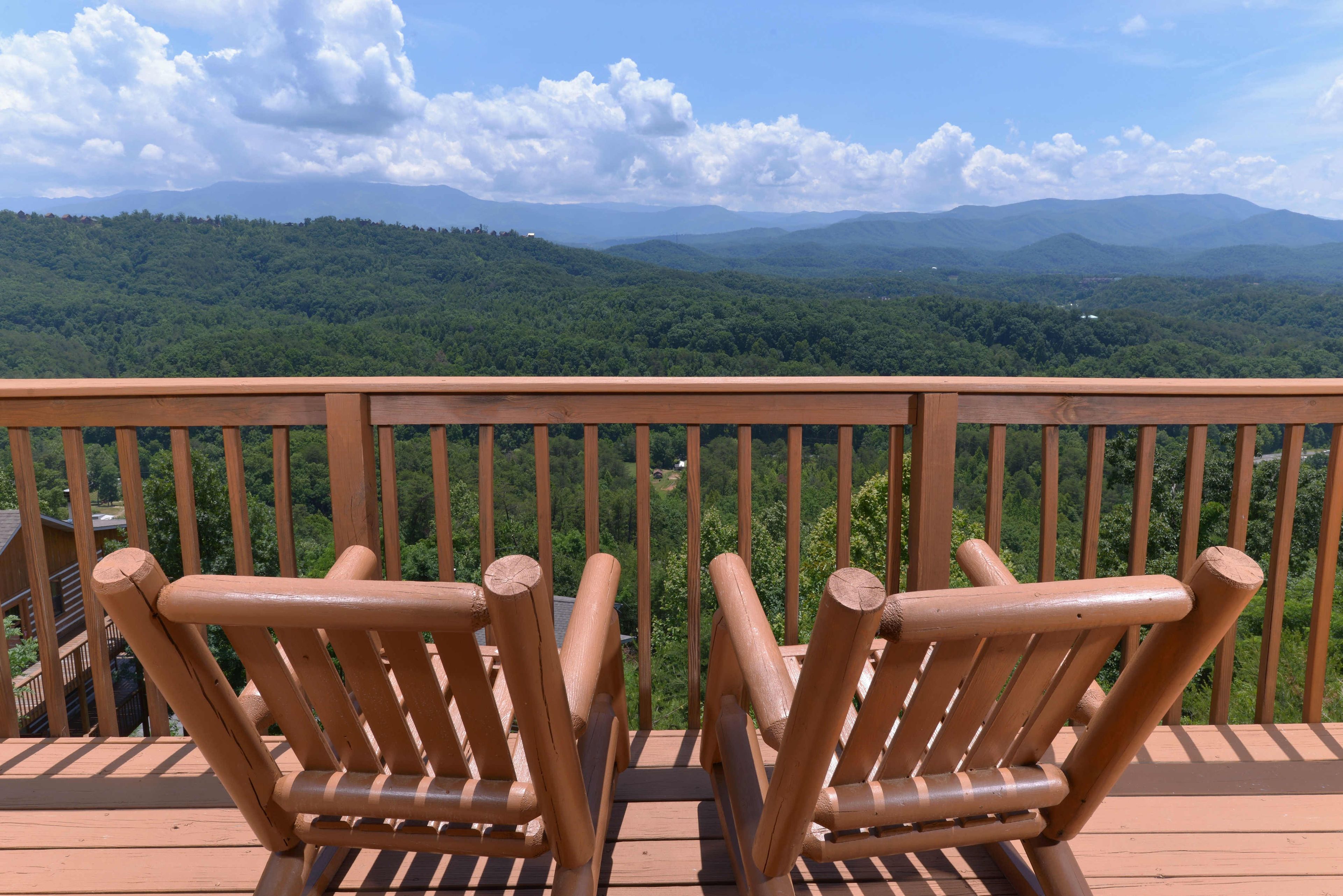 A wooden deck with two wooden chairs facing a scenic view of a forested mountain range.