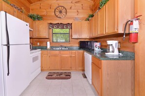 A kitchen with wooden cabinets, a refrigerator, a microwave, a coffee maker, and a fire extinguisher. - Great Mountain View | Next to Dollywood | Pool Table | Pet Friendly | Hot Tub (Pigeon Forge)