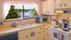 A kitchen with a window view of a lake and trees, white cabinets, a microwave, a toaster, and a stove. - San Juan Island, Roche Harbor Heights #122 (Friday Harbor)