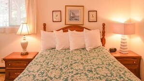 A bedroom with a wooden bed, floral bedding, two bedside lamps, and framed pictures on the wall. - San Juan Island, Roche Harbor Heights #122 (Friday Harbor)