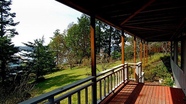 A wooden deck with a railing, overlooking a grassy area with trees and a body of water. - San Juan Island, Roche Harbor Heights #122 (Friday Harbor)