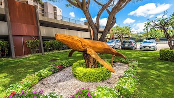 A sculpture of a whale in a landscaped garden with a building in the background.