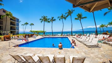 A pool area with lounge chairs and a view of the ocean.