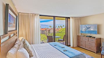Habitación de hotel con cama, televisor, cómoda y balcón con vistas a palmeras y casas.