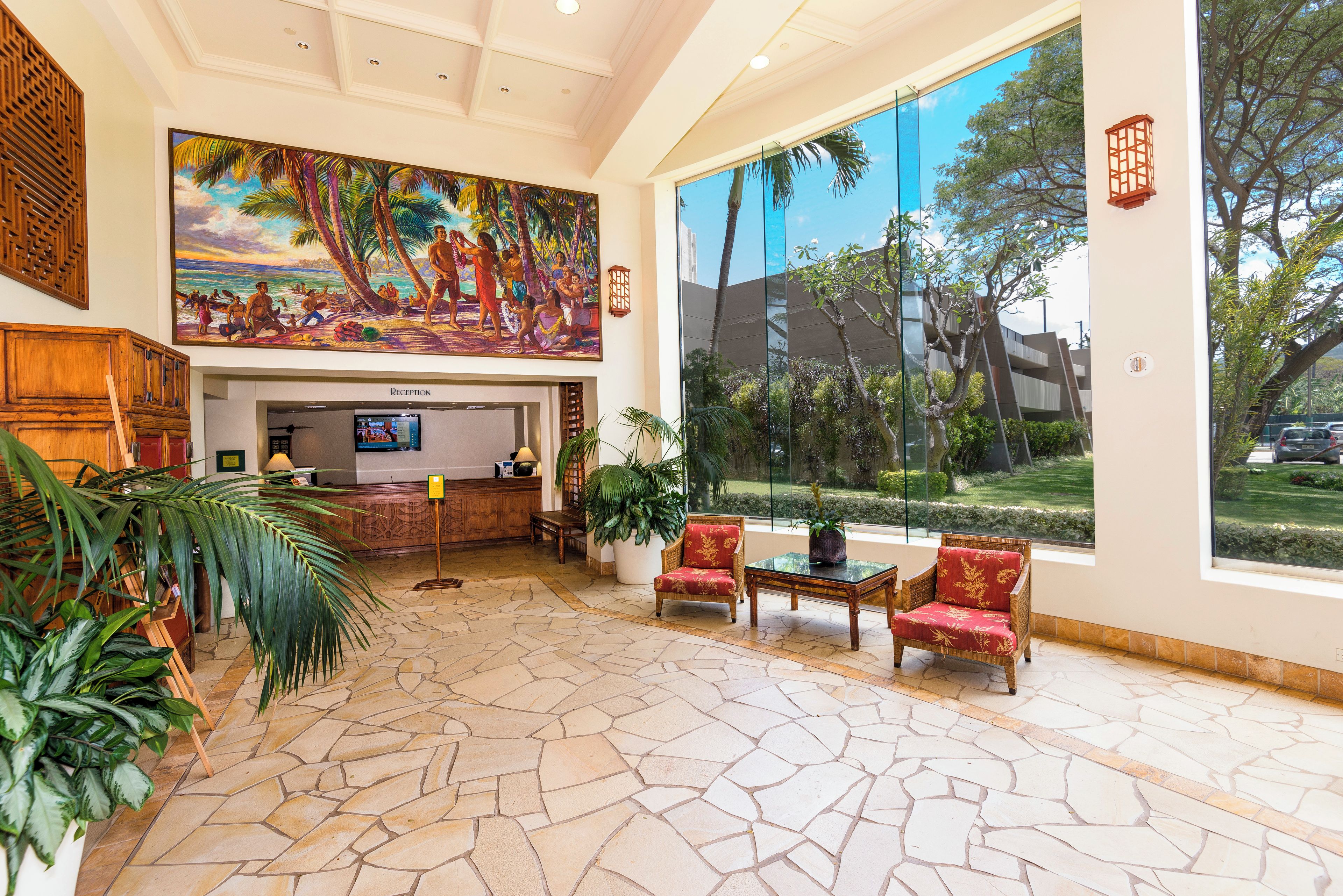 Eine Lobby mit Rezeption, Sitzgelegenheiten, großen Fenstern und tropischer Kunst.