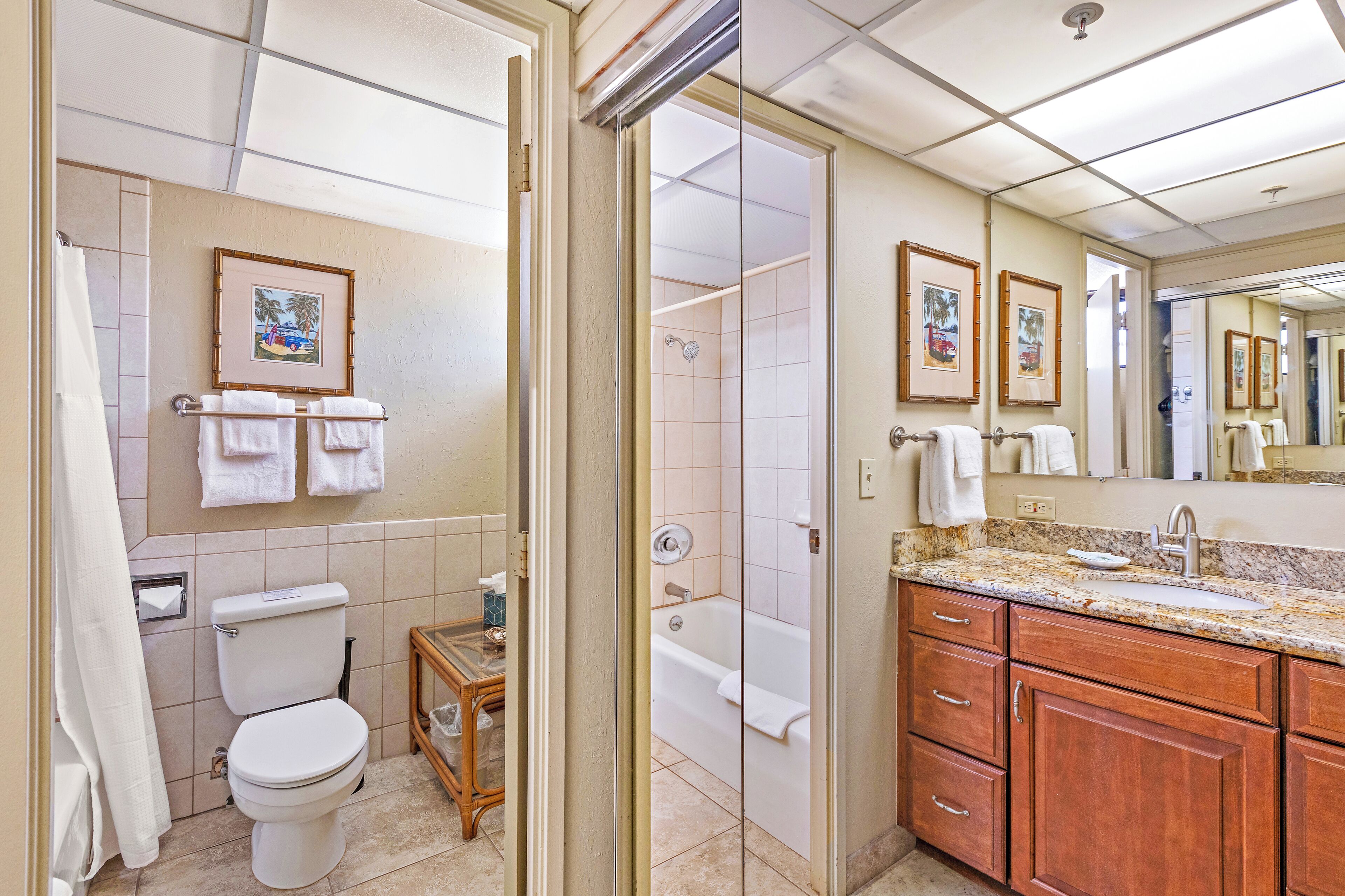 A bathroom with a toilet, sink, and bathtub. There are towels hanging on the wall and a small table with toiletries.