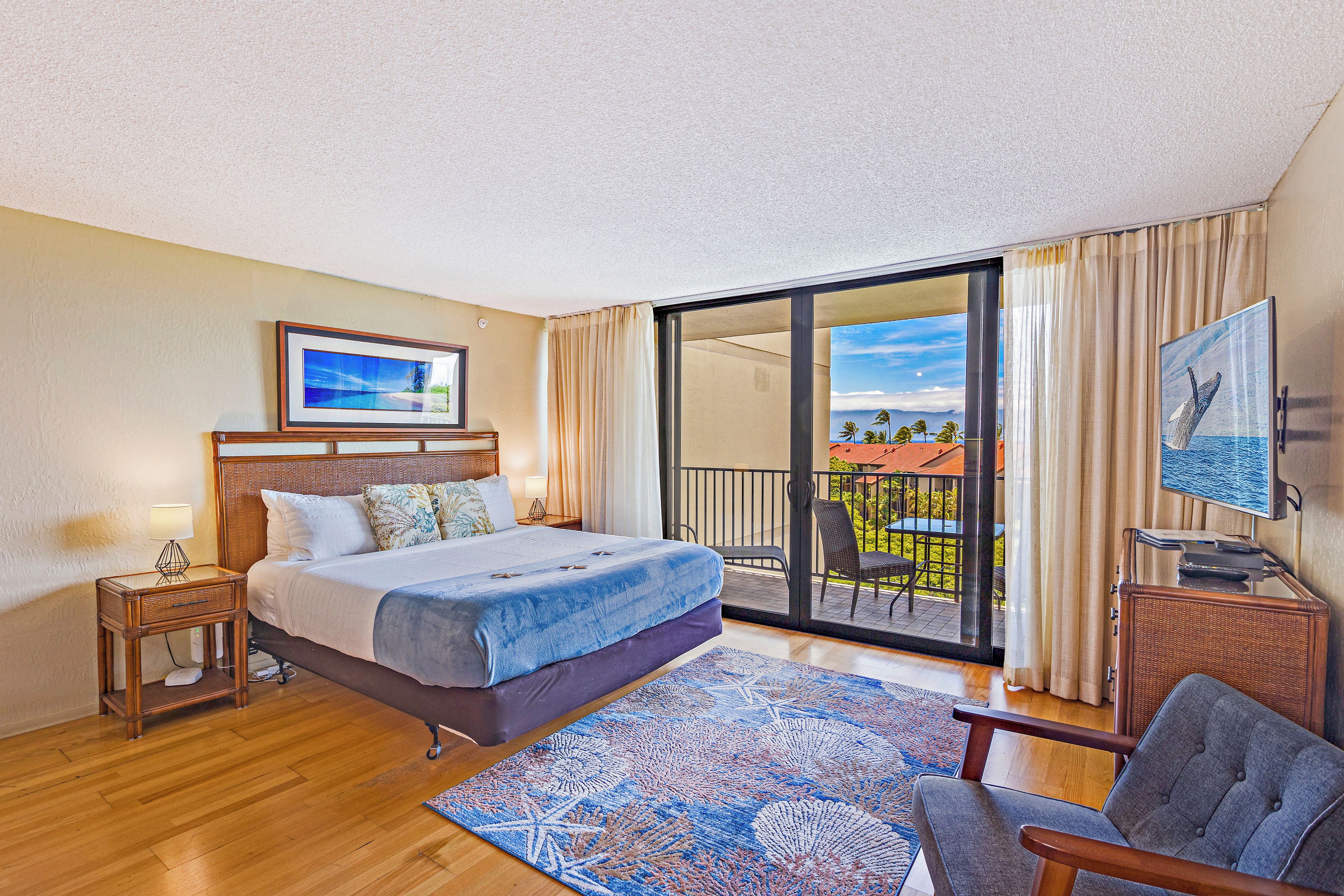 Habitación de hotel con cama, televisión, silla, balcón con vistas y ventana con cortinas.